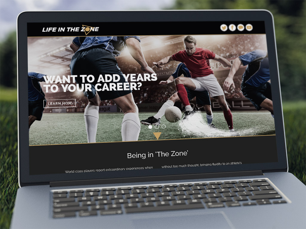 A laptop on the grass in a park displaying the Life in the Zone website