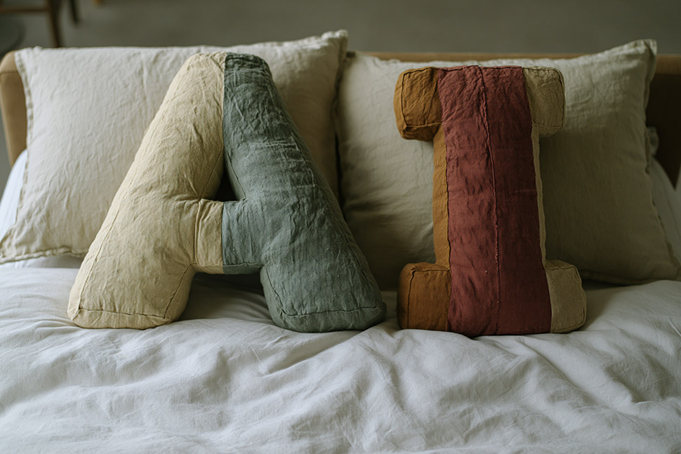 Cushions in the shape of the word 'AI' placed on pillows on a made bed